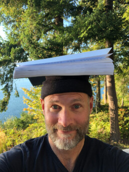 Craig Holt with a book on his head, in front of some trees